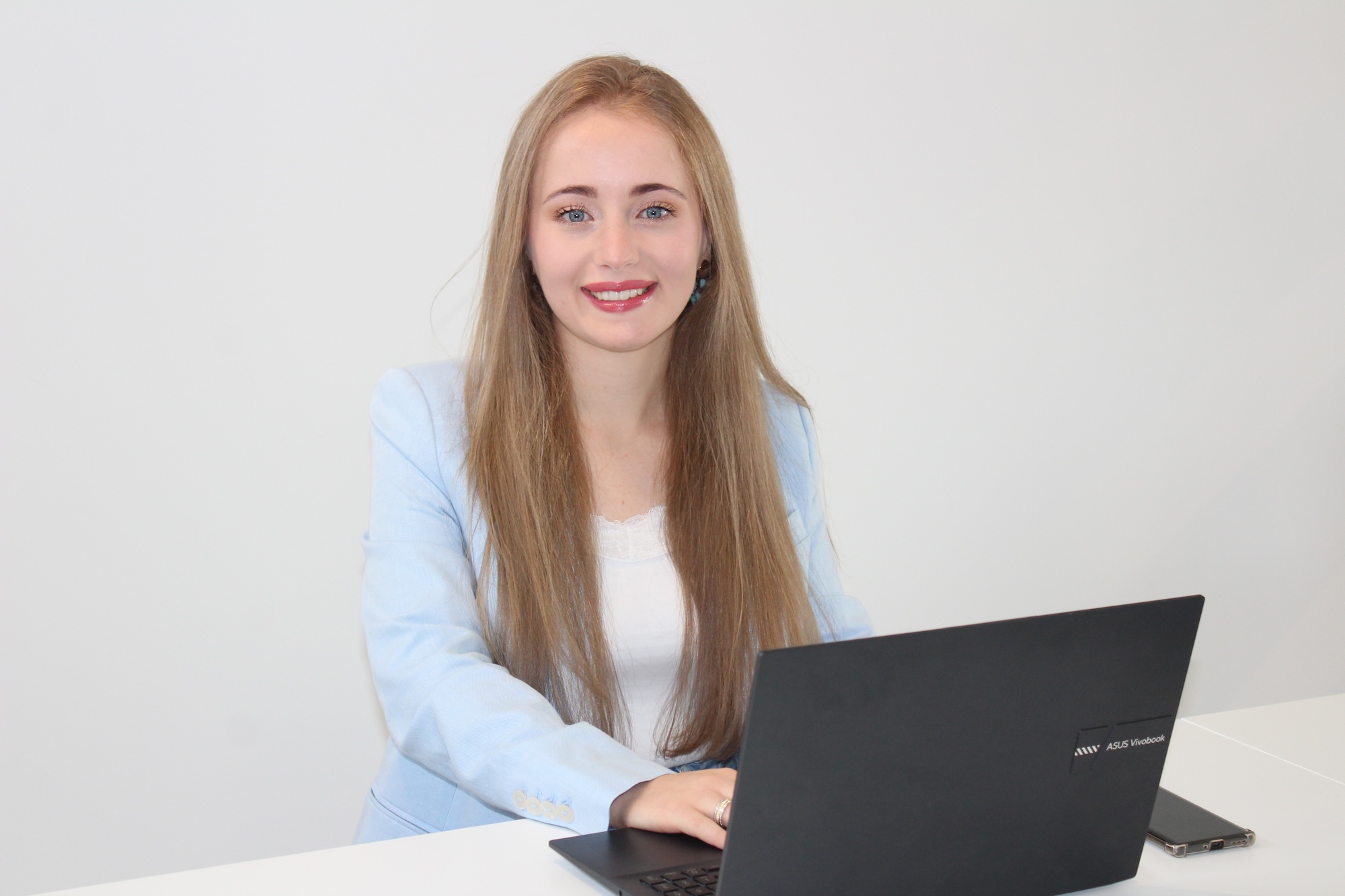 Smiling contact person behind a laptop, looking directly at the camera.
